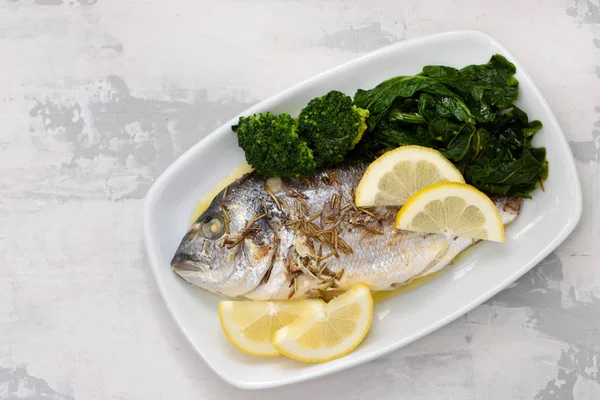 Pesce al forno con limone e verdure in piatto bianco su ba ceramica — Foto Stock