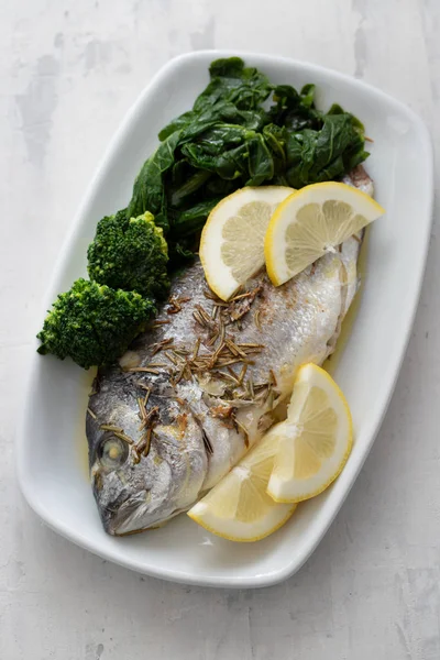 Gebackener Fisch mit Zitrone in weißer Schale auf keramischem Hintergrund — Stockfoto