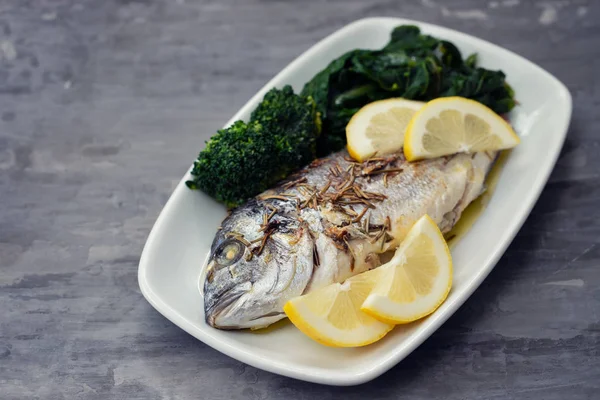 Gebackener Fisch mit Zitrone in weißer Schale auf keramischem Hintergrund — Stockfoto
