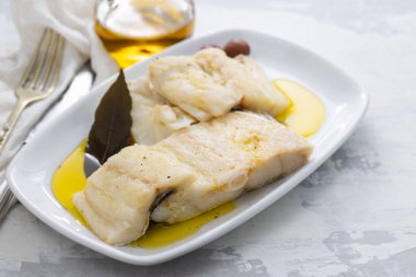 cer üzerinde beyaz çanak üzerinde defne yaprağı ve zeytinyağı ile haşlanmış morina balığı