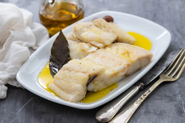 Pescado de bacalao cocido con hoja de laurel y aceite de oliva en plato blanco en cer —  Fotos de Stock