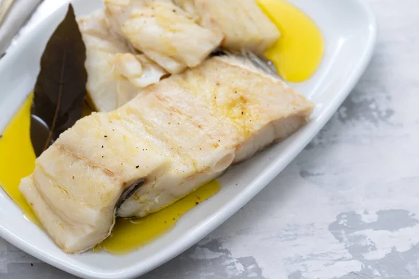 Pescado de bacalao cocido con hoja de laurel y aceite de oliva en plato blanco en cer — Foto de Stock