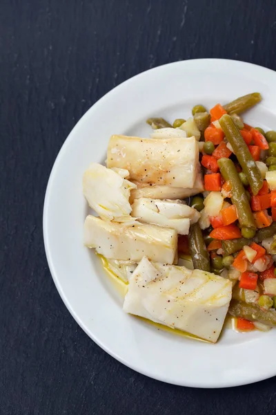 Boiled cod fish with boiled vegetables on white plate on black c — Stock Photo, Image