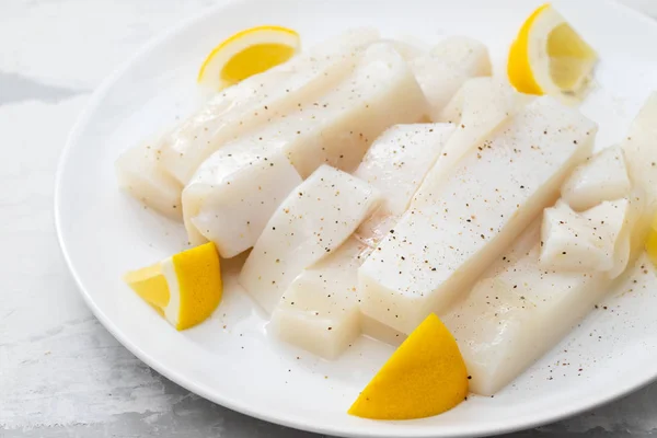Raw squid with pepper and fresh lemon on white plate — Stock Photo, Image
