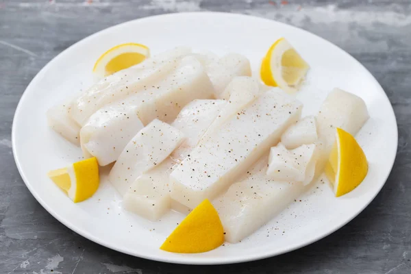 Raw squid with pepper and fresh lemon on white plate — Stock Photo, Image