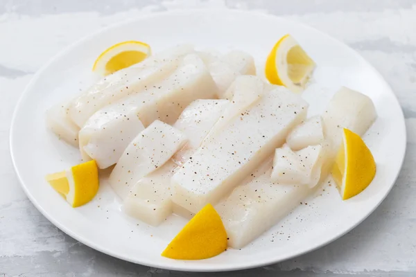 Raw squid with pepper and fresh lemon on white plate — Stock Photo, Image