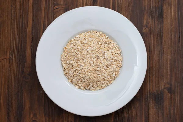 Uncooked oats in white plate on wooden background — Stock Photo, Image