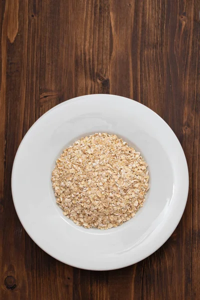 Uncooked oats in white plate on wooden background — Stock Photo, Image