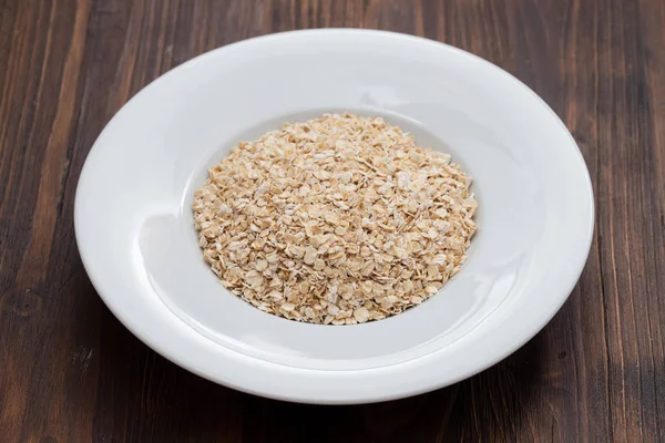 Avena cruda en plato blanco sobre fondo de madera —  Fotos de Stock