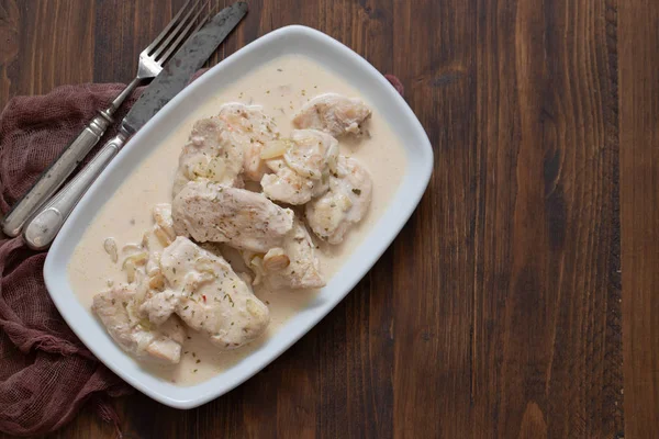 Chicken with creamy sauce on dish on brown wooden background — Stock Photo, Image