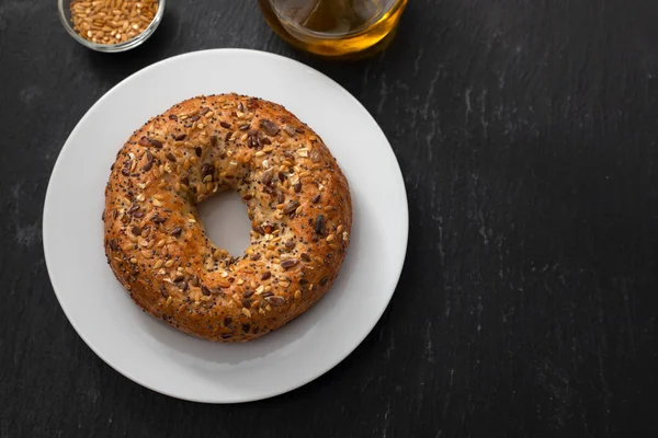 Färsk bagel med frön på vit plåt på keramisk bakgrund — Stockfoto