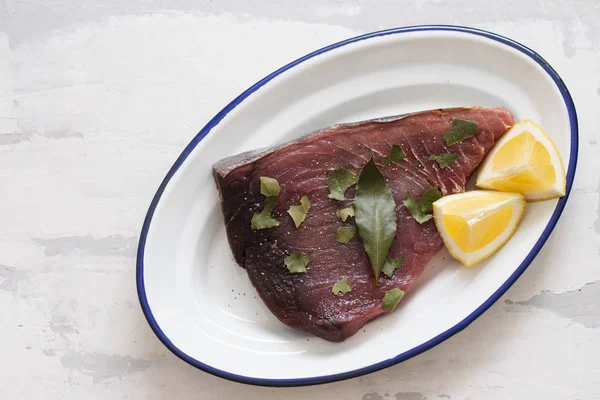 Rauwe tonijn met citroen en laurierblad op keramische achtergrond — Stockfoto