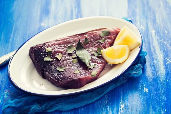 Rauwe tonijn met citroen en laurierblad op keramische achtergrond — Stockfoto
