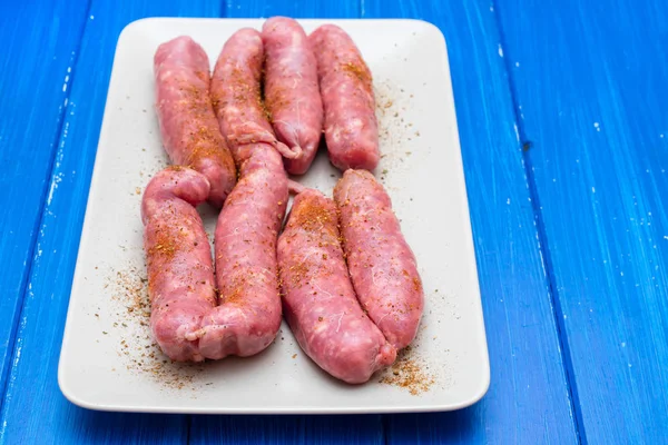 Raw sausages on dish on wooden background — Stock Photo, Image