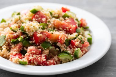 Beyaz tabakta kuskus olan taze sebze salatası.