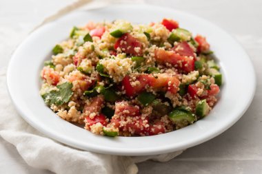 Beyaz tabakta kuskus olan taze sebze salatası.