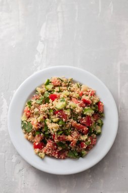 Beyaz tabakta kuskus olan taze sebze salatası.