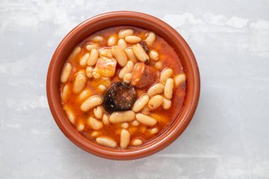 Tipik İspanyol yemeği masalı, füme sosisli fasulye ve kahverengi seramik tabakta et.