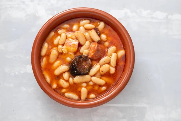 Tipik İspanyol yemeği masalı, füme sosisli fasulye ve kahverengi seramik tabakta et.