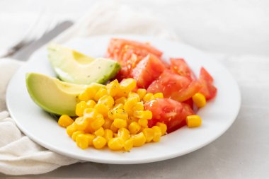Mısır, domates ve beyaz tabakta avokado salatası.