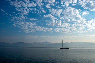 Parlak deniz ve yelkenli bulutlu gökyüzünün altında