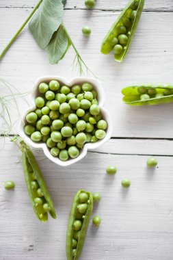Beyaz ahşap masa üzerinde beyaz kase soyulmuş taze yeşil bezelye