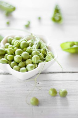 Beyaz ahşap masa üzerinde beyaz kase soyulmuş taze yeşil bezelye