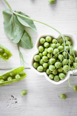 Beyaz ahşap masa üzerinde beyaz kase soyulmuş taze yeşil bezelye