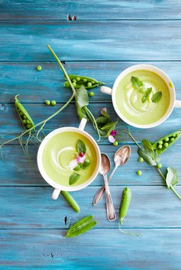 Mavi ahşap zemin üzerine kaşık krem yeşil bezelye çorbası