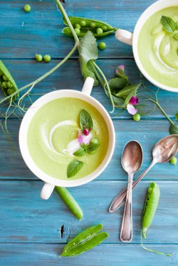 Mavi ahşap zemin üzerine kaşık krem yeşil bezelye çorbası