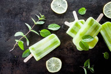 Limon dilimleri ve nane yaprakları ile karanlık tabloda sağlıklı malzemelerle yapılmış çubuklu dondurmayı görünümü Kapat