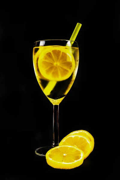 Tranches de citron dans une boisson transparente dans un verre sur un fond noir — Photo