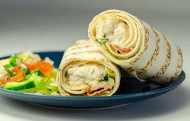Tavuklu tortilla dürümü ve kayın ağacı tütsülenmiş domuz pastırması mavi tabakta karışık salatayla servis edilir. Lezzetli yemek.
