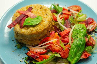 Eriyen çedar soslu füme mezgit balığı keki ve mavi tabakta karışık salata, deniz ürünleri.