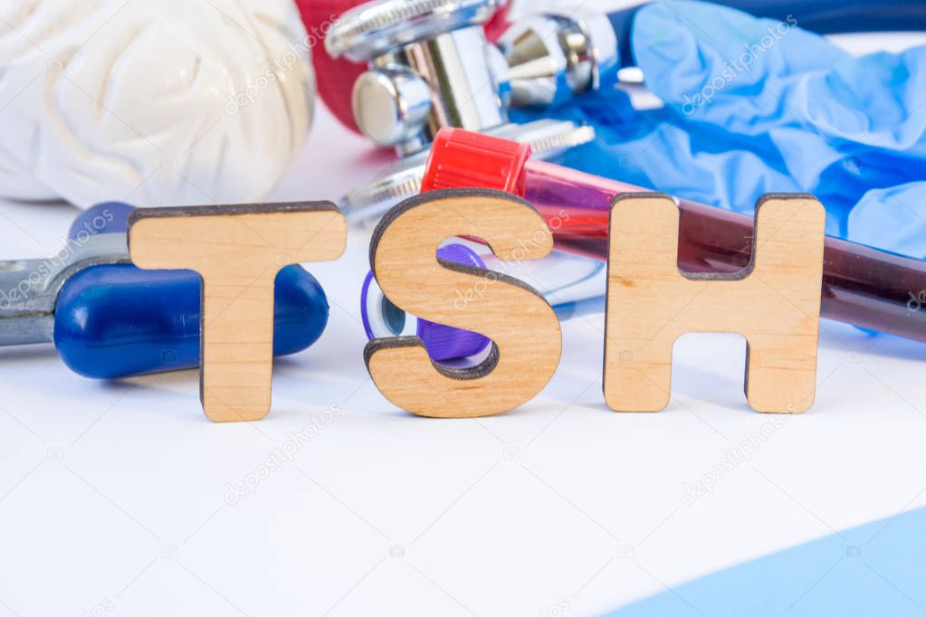 TSH abbreviation or acronym in foreground in laboratory scientific or medical practice meaning thyroid stimulating hormone, with model of brain, neurological hammer, laboratory test tubes, stethoscope