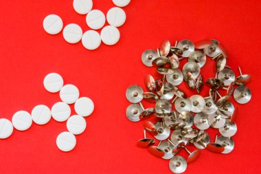 Arrows of pills as a pharmacological agent painkiller and sharp metal thumbtacks as a symbol of pain on red background. Concept photo of action of painkillers or analgesic (anesthetics) in human body clipart