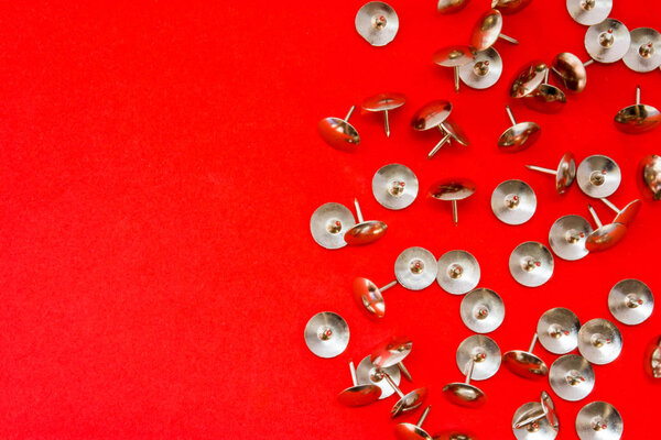 Metal shiny sharp pins or thumbtracks scattered on red background with clean area of photo for labels or headers. Symbol of symptom of acute pain, disease, hemorrhoids in proctology, dangers, hard way