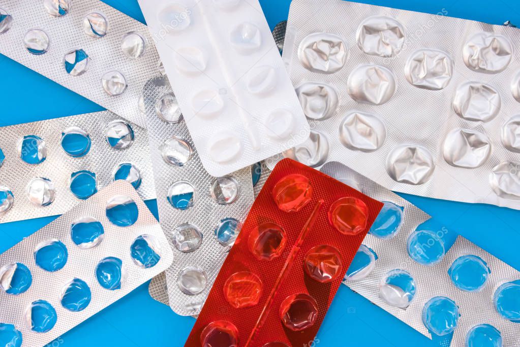 A lot of empty plastic blister packaging of pharmaceutical tablets and pills on blue background. Concept of end of treatment, the lack of medicines in the pharmacy or the impossibility to get them