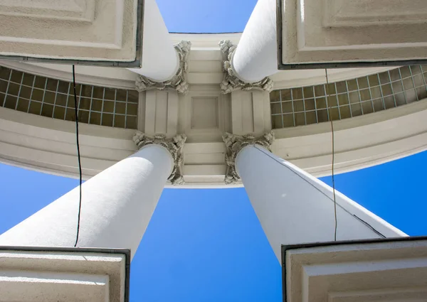 The architecture of the Empire style. Four big concrete columns with bases in the corners of the photo hold the roof against the blue sky bottom view