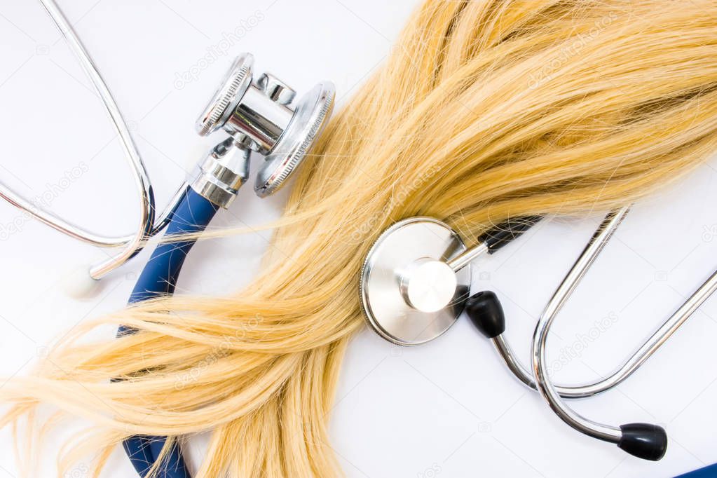 Medical concept in trichology, dermatology and hair examination. Curl or lock of blonde hair of patient  is surrounded by two heads of stethoscopes, which examined it top view