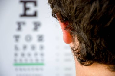 Concept photo of myopia or nearsightedness as diseases of eye and the optical system. In the background blurry fuzzy table for testing visual acuity, in the front - head of the person in focus closeup clipart