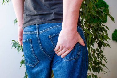 Adam kalçanın alt kısmında elini tutar. Siyatik sinir çıkışında ağrı kavramı fotoğraf belirtileri, inflamasyon, omurga siyatik veya osteokondroz, gluteus kas ağrısı, rektum veya anüs  