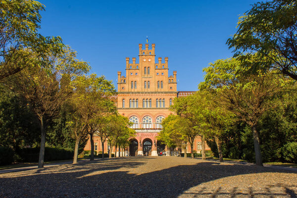 Photo of main building of University from entrance gate on blue autumn sky and yellow and green foliage on trees. Architecture of the University of Chernivtsi