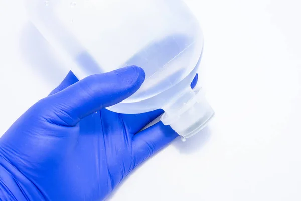 护士或医疗专业人员手握一只胶乳手套 这是一个装有输液液的塑料瓶 用于在急诊期间静脉注射病人 — 图库照片