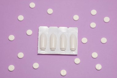 Vajinal ya da rektal fitilli plastik ambalaj mor arka planda polka noktalarıyla süslenmiş yuvarlak tabletlerle çevrilidir. Proktolojik ya da jinekolojik fotoğraf tedavisi kavramı