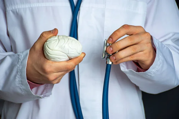 Concept photo of diagnosis in neurology. Doctor hold in one hand model of human brain, in other stethoscope and conducts diagnostic process and presence of nervous system diseases, mental, dementia