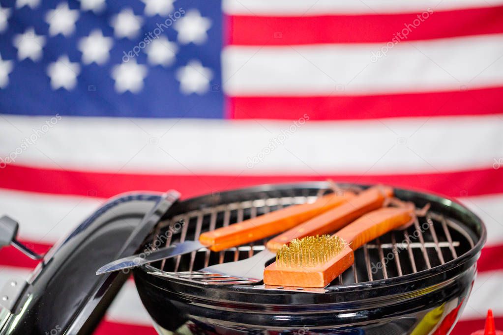 Small round charcoal grill and July 4th decorations on American flag background.