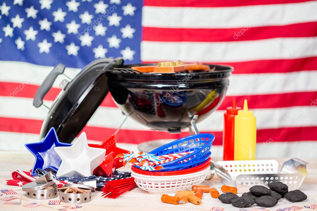 Small round charcoal grill and July 4th decorations on American flag background.