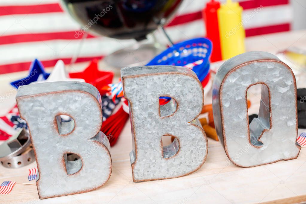 Metal BBQ sign on small round charcoal grill with July 4th decorations.