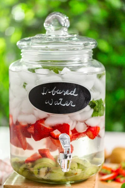 Infused water with organic strawberries, kiwi and fresh mint in glass beverage drink dispenser.